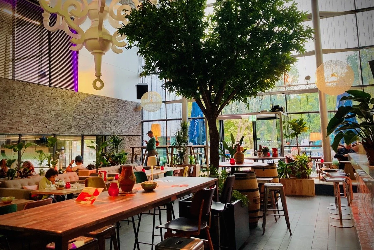 Zaal van Het Plantsoen met grote boom, lange tafels en veel daglicht
