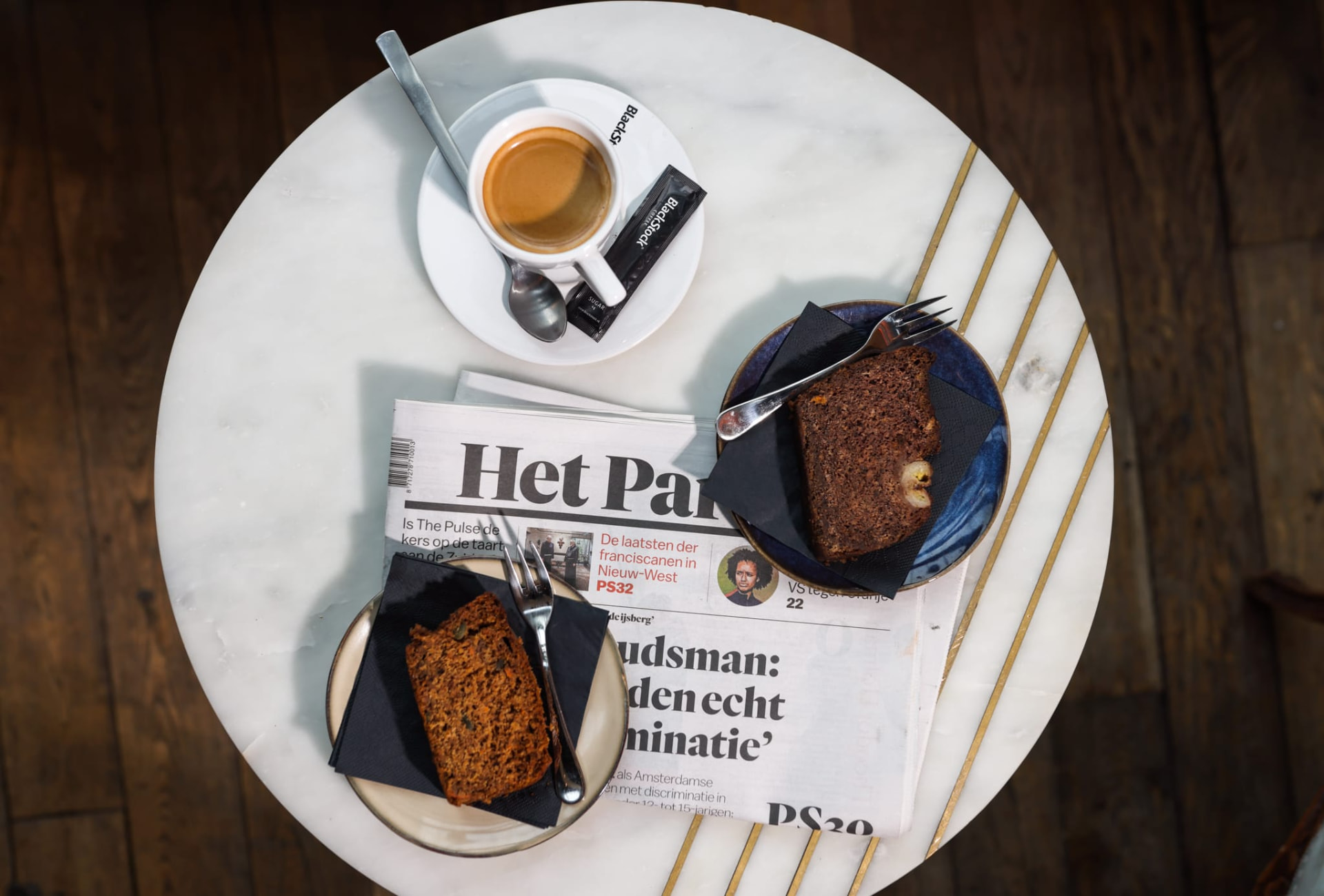 Koffie met cake en de krant op een marmeren tafeltje bij Het Plantsoen